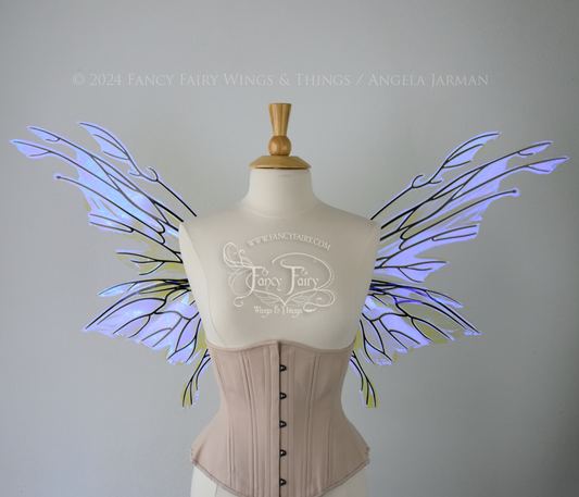 Front view of an ivory dress form wearing an alabaster underbust corset & large violet iridescent fairy wings with elongated upper panels with petal like appendages at the tips & antennae, the veins are black