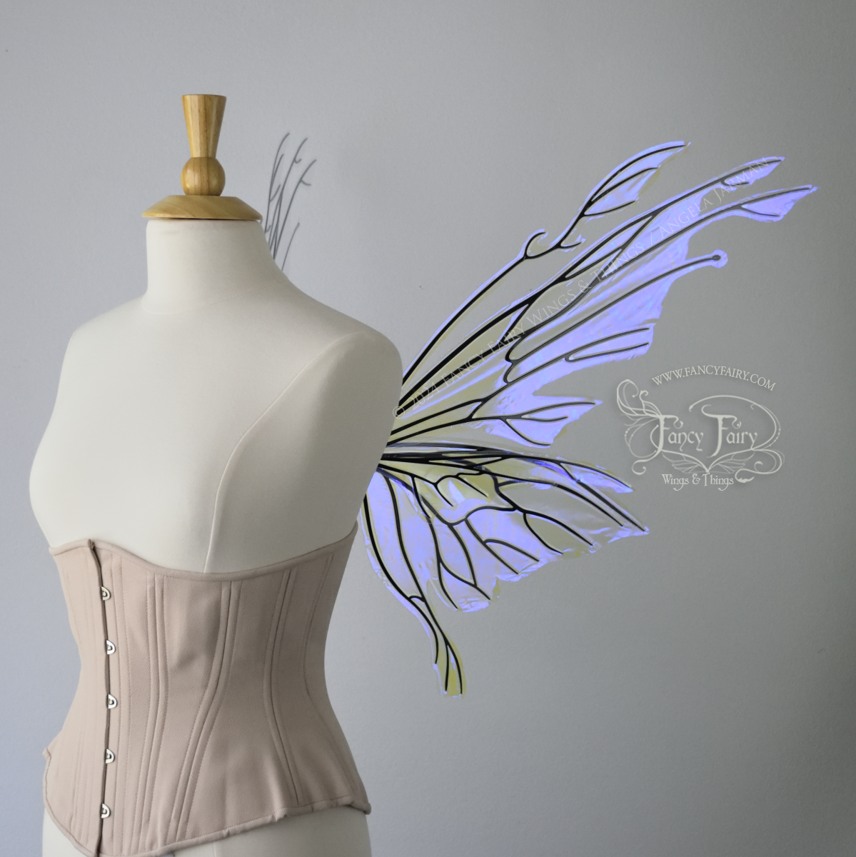 Right side view of an ivory dress form wearing an alabaster underbust corset & large violet iridescent fairy wings with elongated upper panels with petal like appendages at the tips & antennae, the veins are black