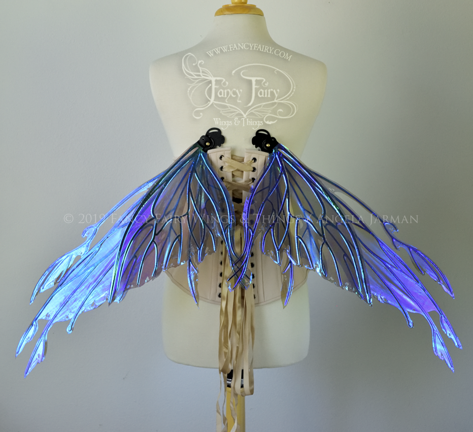 Back view of an ivory dress form wearing an alabaster underbust corset & violet blue 'Dark Crystal' iridescent fairy wings in resting position with elongated upper panels with petal like appendages at the tips & antennae, the veins are black