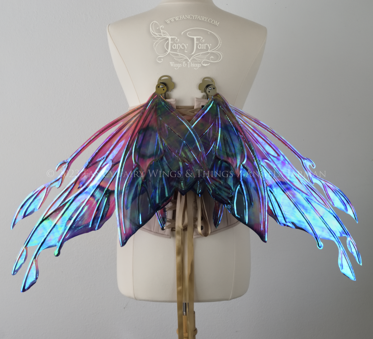 Back view of an ivory dress form wearing an underbust corset & 'Goblin Princess' magenta & blue painted iridescent wings w/ gold veins, in resting position