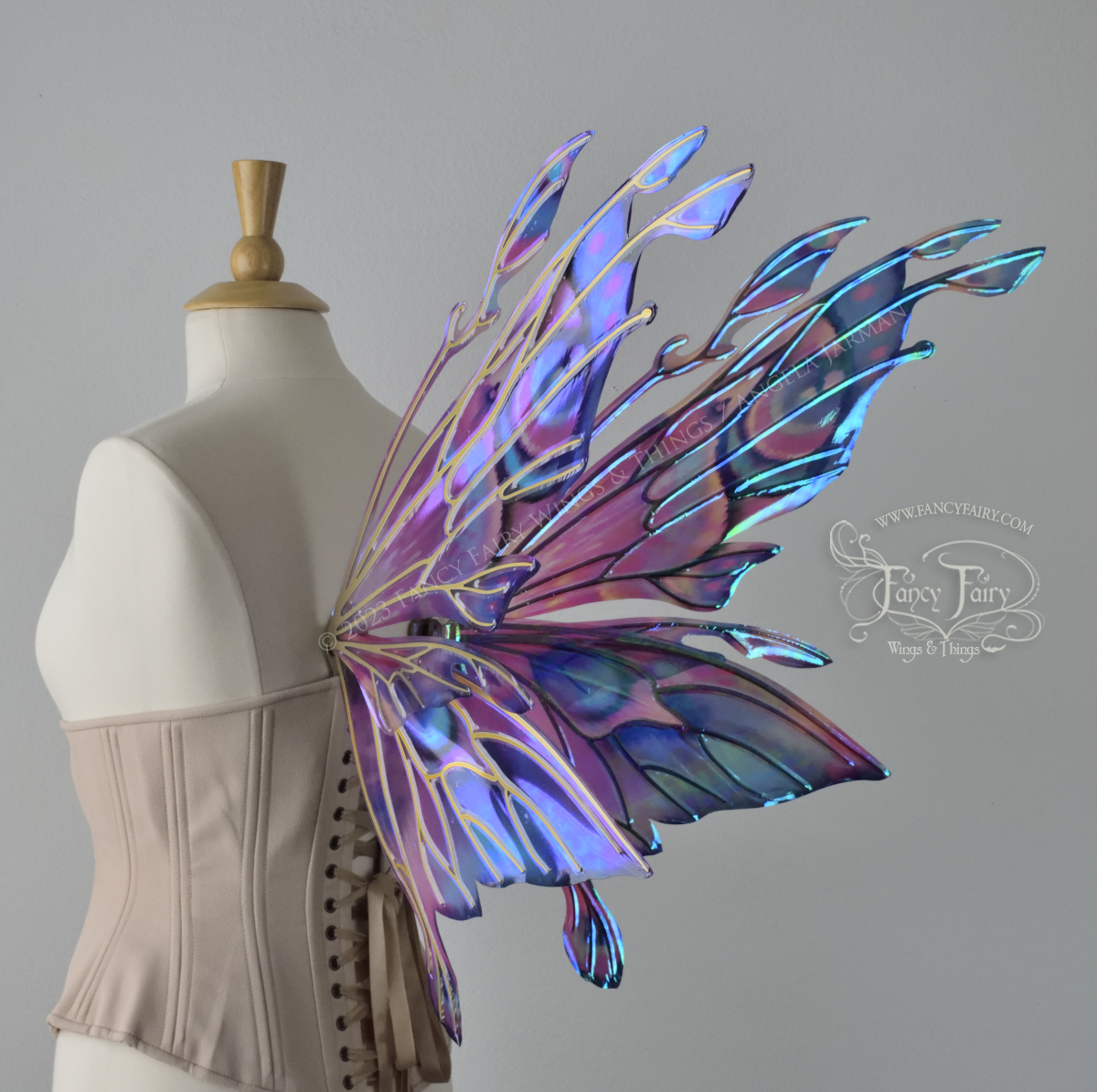 Back 3/4 view of an ivory dress form wearing an underbust corset & 'Goblin Princess' magenta & blue painted iridescent wings w/ gold veins 