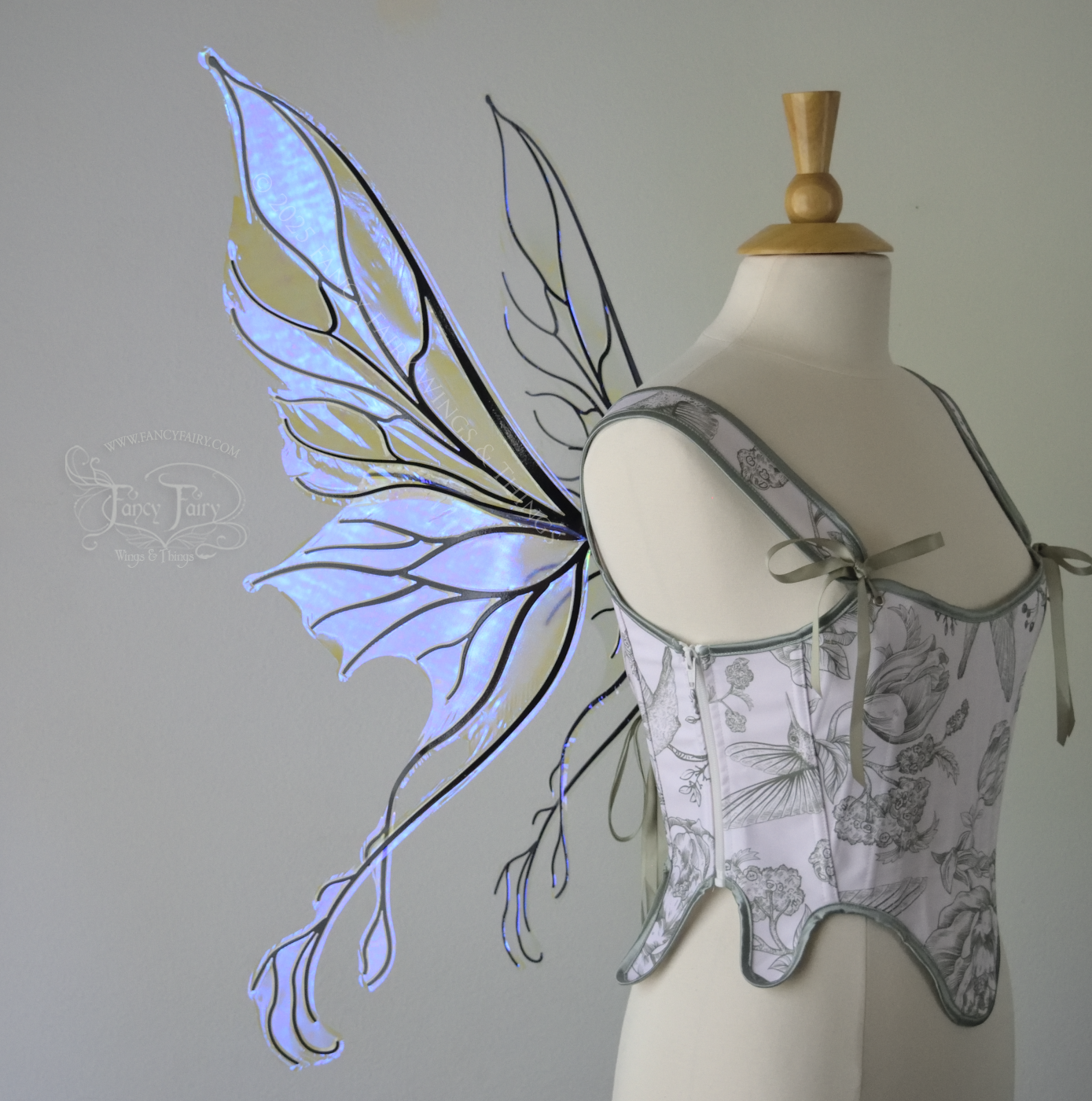Violet iridescent fairy wings with pointed upper tips and 2 swirling tails on the bottom panels with black veins, worn on a dress form, left side view