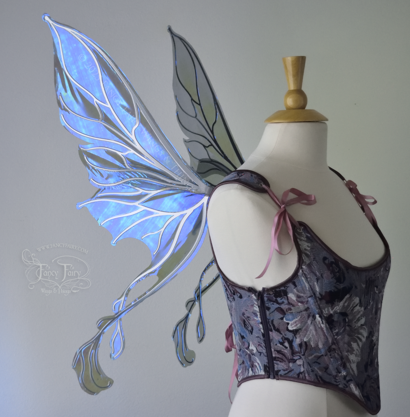 Transparent blue / purple / grey iridescent fairy wings with pointed upper tips and 2 swirling tails on the bottom panels with silver veins, worn on a dress form, left side view