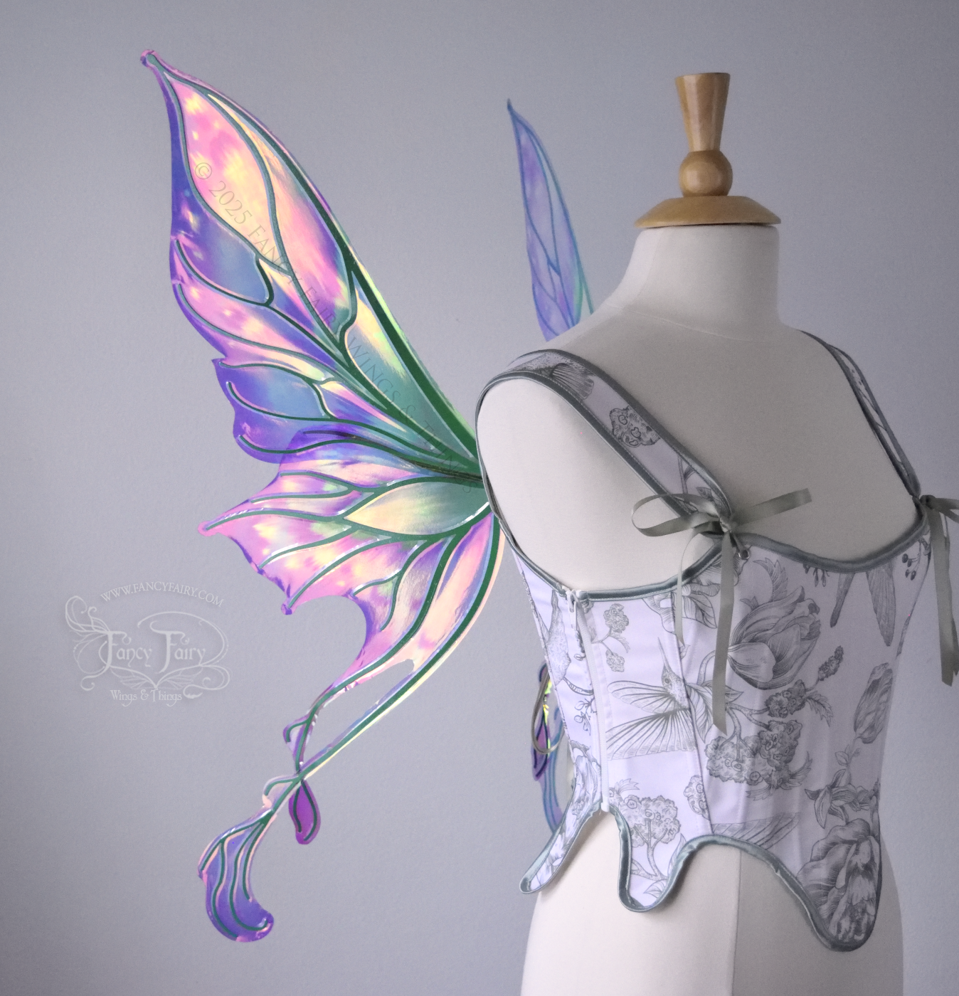 Magenta and green iridescent fairy wings with pointed upper tips and 2 swirling tails on the bottom panels with green veins, worn on a dress form, left side view