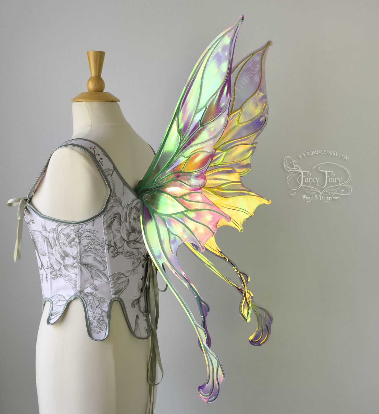Painted iridescent fairy wings with pointed upper tips and 2 swirling tails on the bottom panels with green veins, worn on a dress form, back 3/4 view