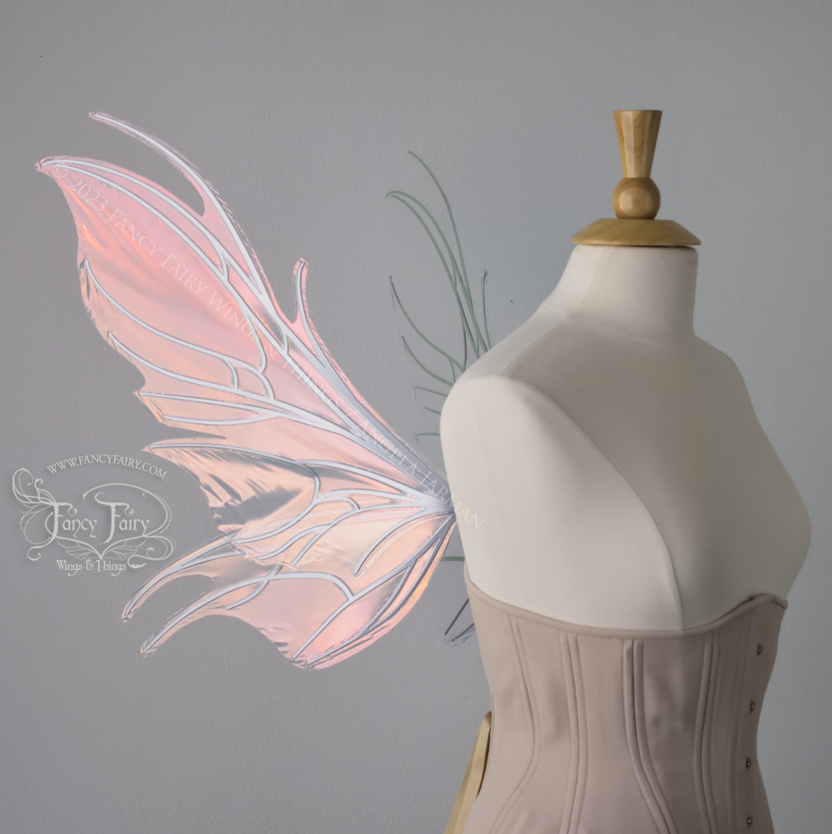 Left side view of a dress form wearing an underbust corset & pink iridescent fairy wings with a spikey shape, with silver veins