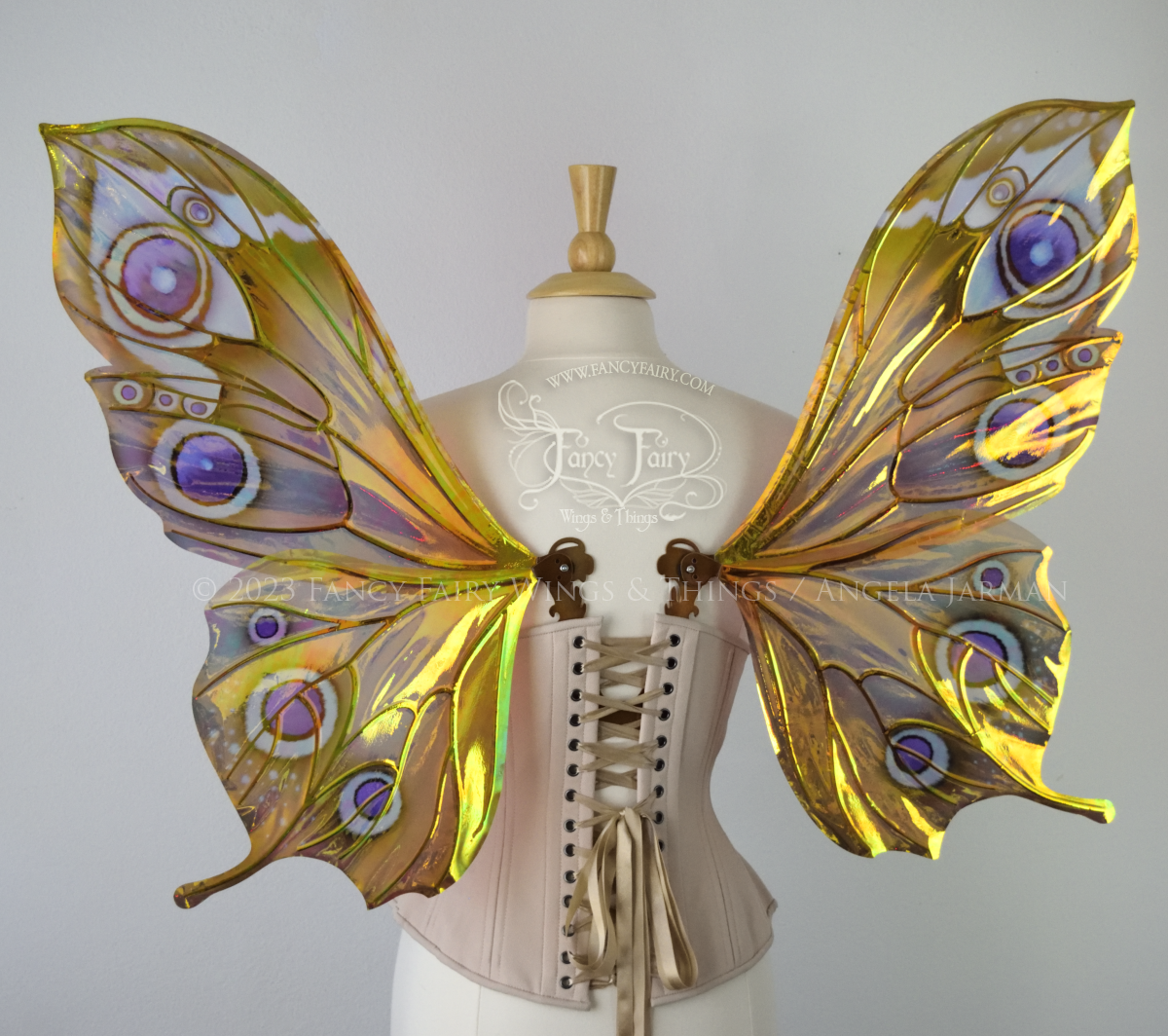 Back view of iridescent butterfly-shaped fairy wings painted with warm autumn colors & purple and black 'eye' spots, worn on a dress form