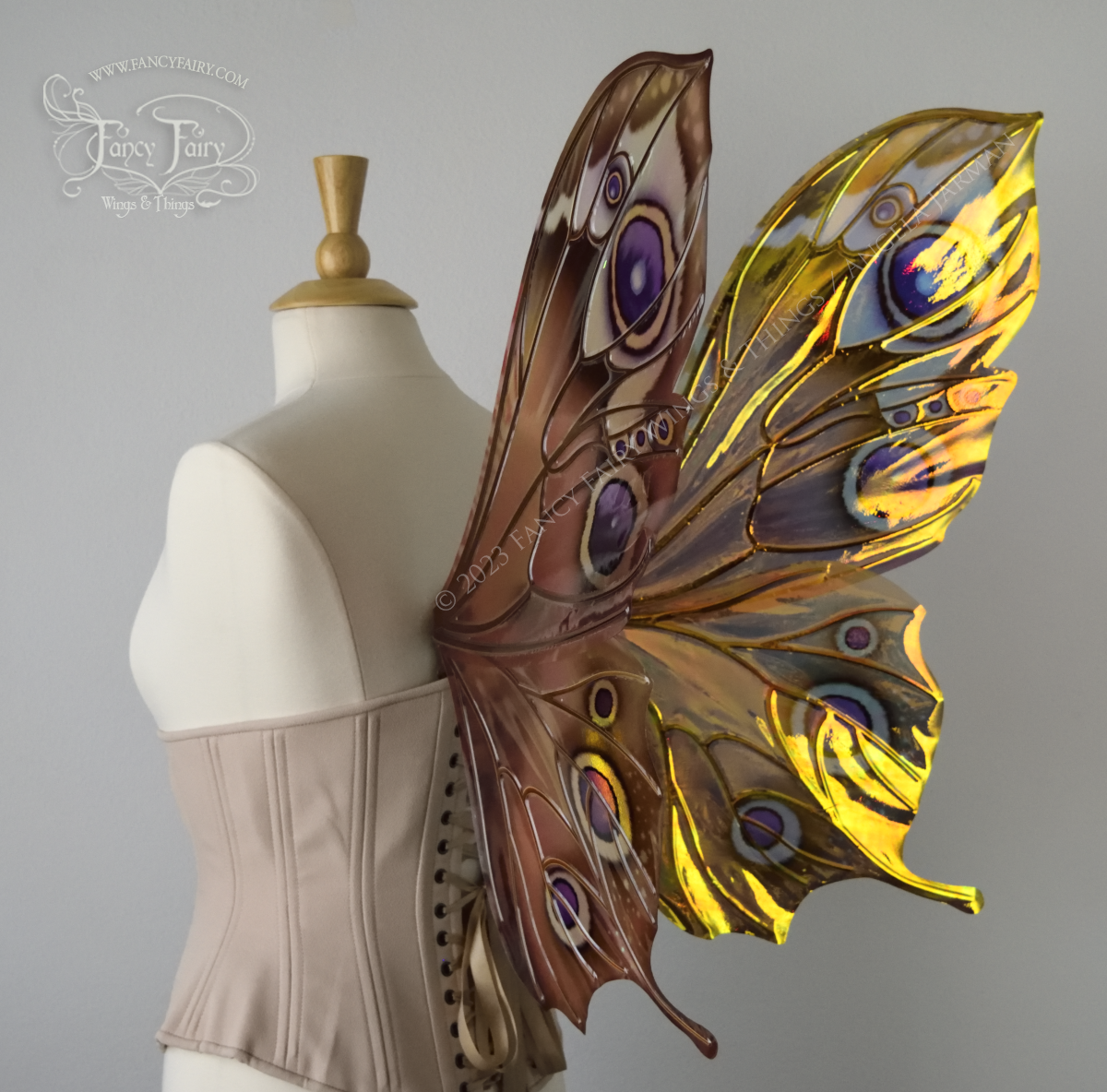 Back 3/4 view of iridescent butterfly-shaped fairy wings painted with warm autumn colors & purple and black 'eye' spots, worn on a dress form