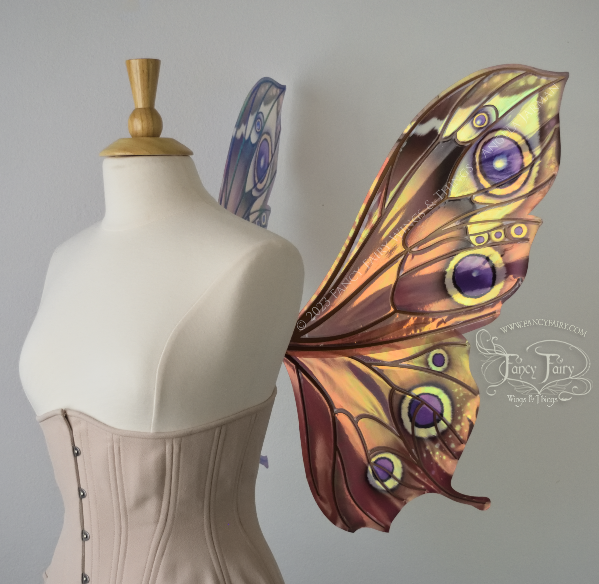 Right side view of iridescent butterfly-shaped fairy wings painted with warm autumn colors & purple and black 'eye' spots, worn on a dress form