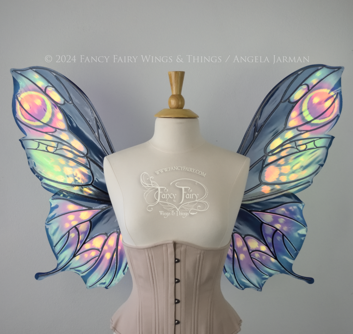 Front view of butterfly shaped iridescent wings in shades of teal with pink and lavender accents with black veins, worn on a dressform