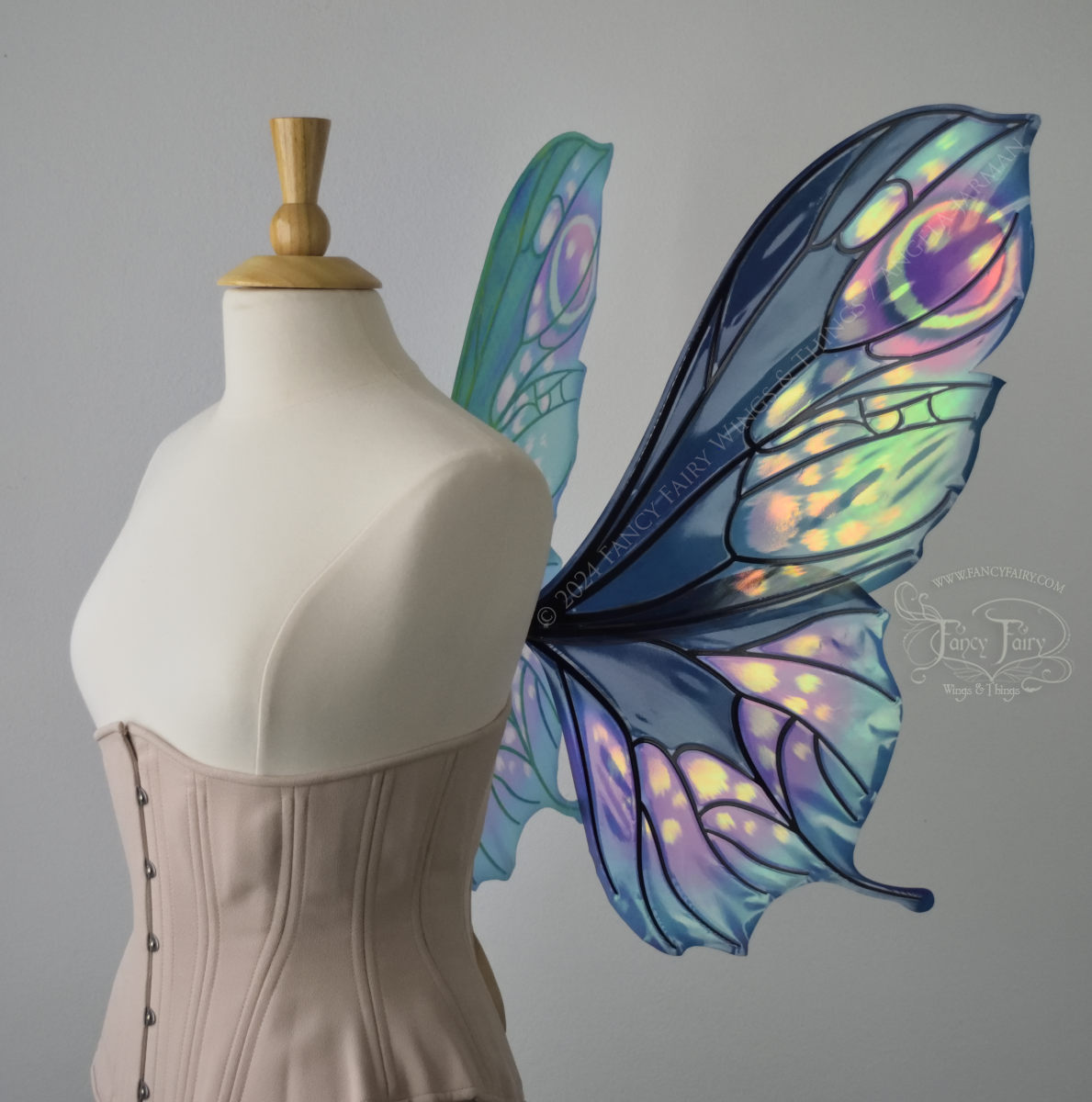 Right side view of butterfly shaped iridescent wings in shades of teal with pink and lavender accents with black veins, worn on a dressform