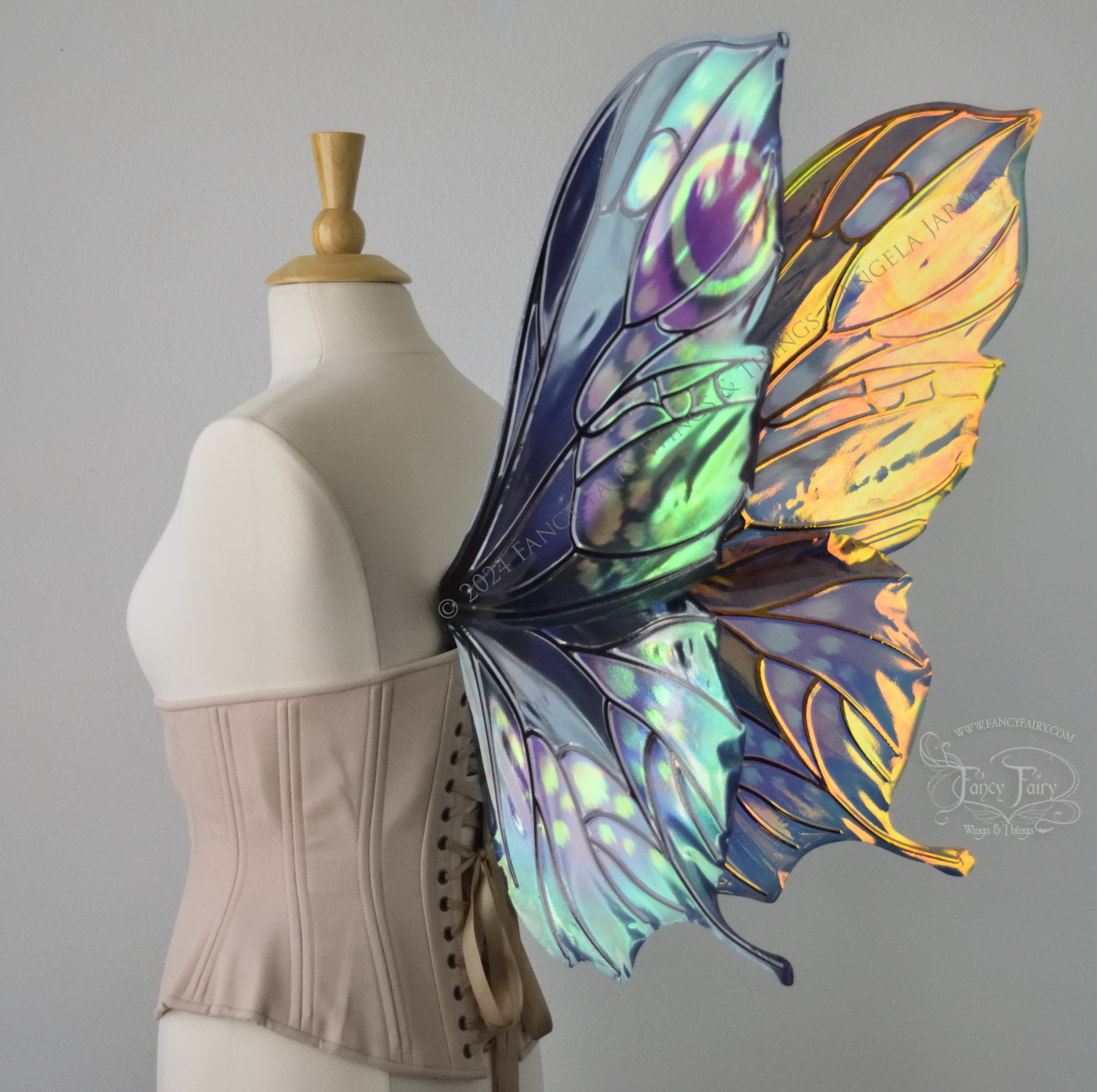 3/4 back view of butterfly shaped iridescent wings in shades of teal with pink and lavender accents with black veins, worn on a dressform