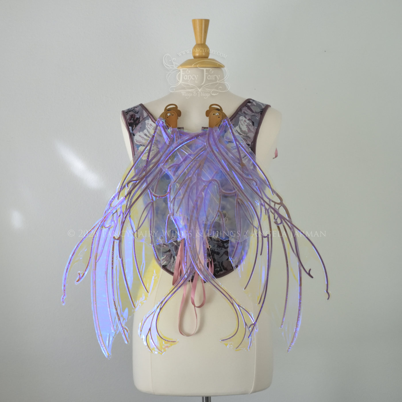 Large violet transparent iridescent fairy wings with a spikey profile and curvy tails on bottom, worn on a dress form, back view in resting position.