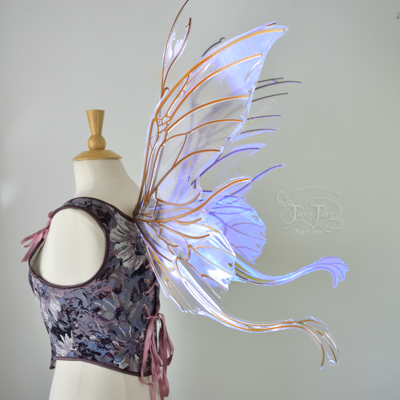 Large violet transparent iridescent fairy wings with a spikey profile and curvy tails on bottom, worn on a dress form, back 3/4 view.