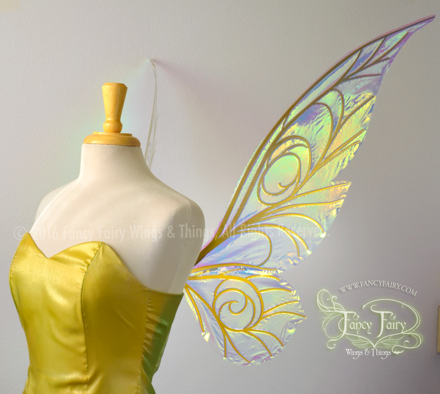 Right side view of an ivory dress form wearing an iridescent green strapless pixie dress & large transparent iridescent fairy wings with spiraling whimsical gold veins & a classic pixie silhouette. Background is white, the Fancy Fairy Wings & Things logo is visible on the right bottom corner