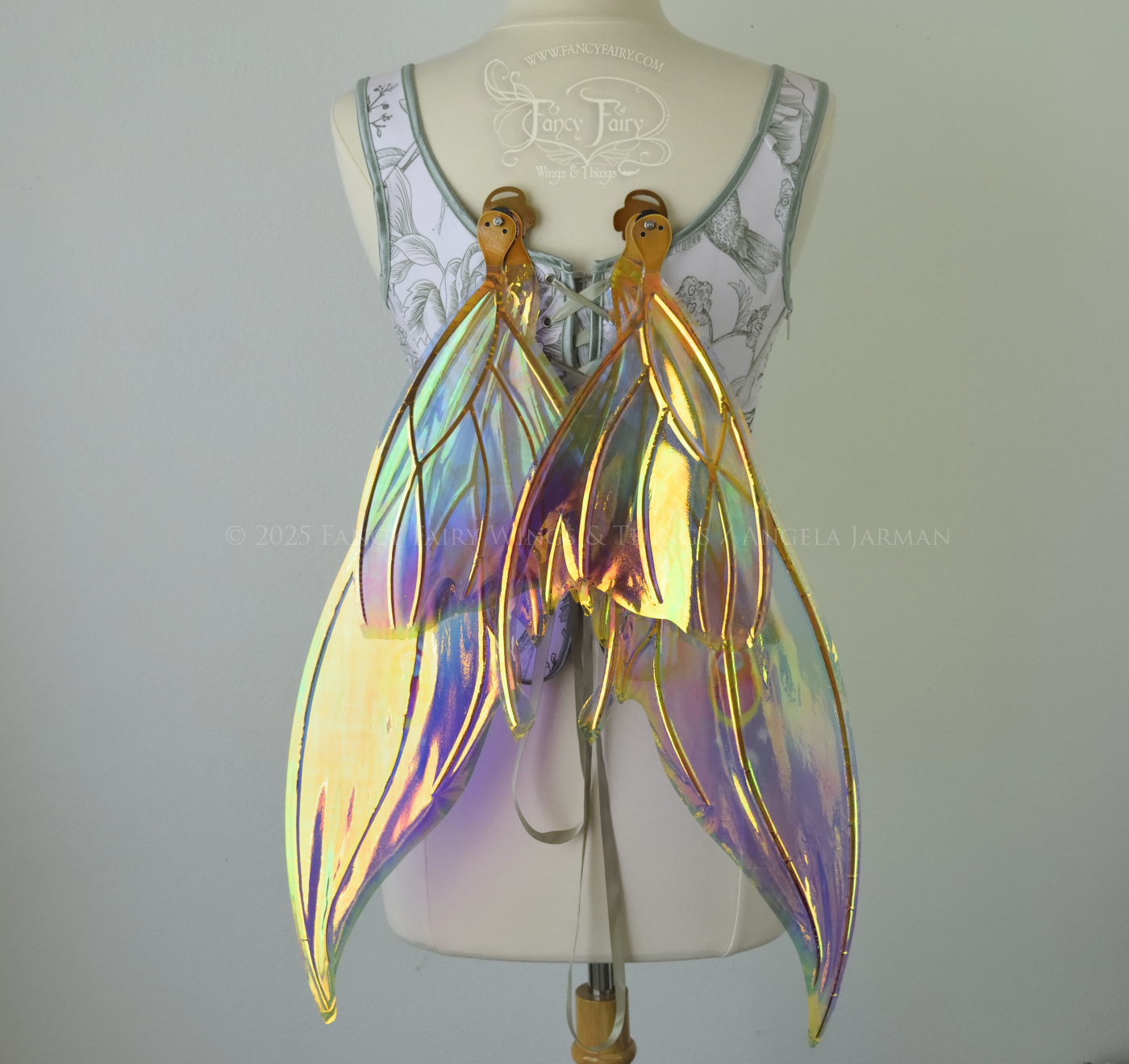 Iridescent rainbow fairy wings with elongated slightly downward curved tips on upper panels, and small tail that swoops up from bottom panels, worn on a dress form, back view, in resting position