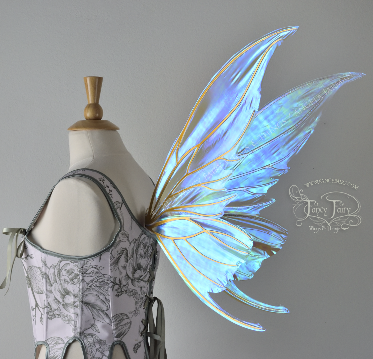 Large blue green iridescent fairy wings with gold veins worn with a white & sage green bodice on a dress form, back 3/4 view