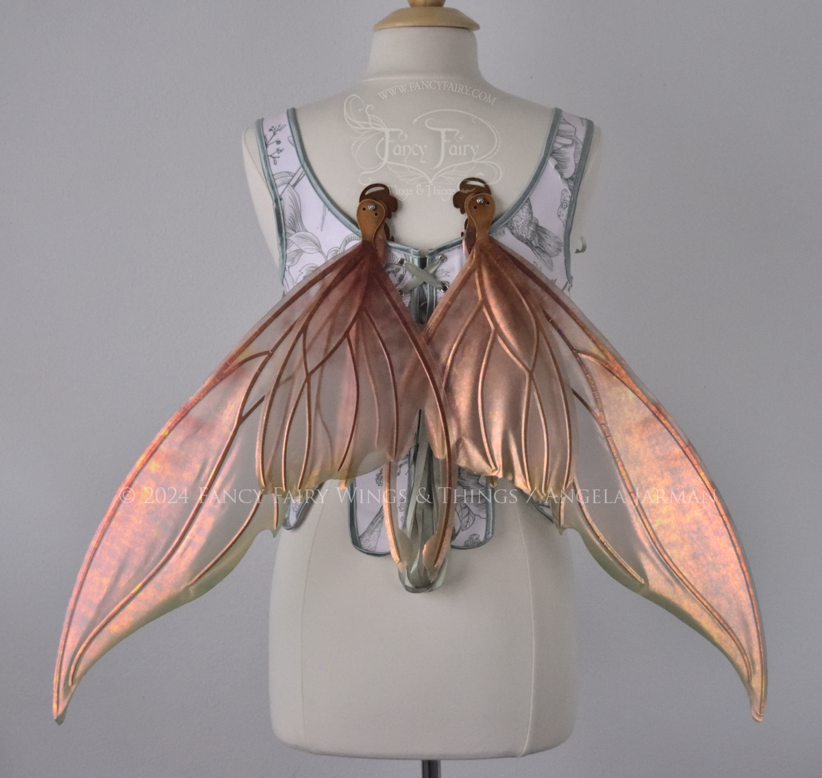 Large coppery iridescent fairy wings with brown and green accents, copper veins, worn with a white & sage green bodice on a dress form, back view, in resting position