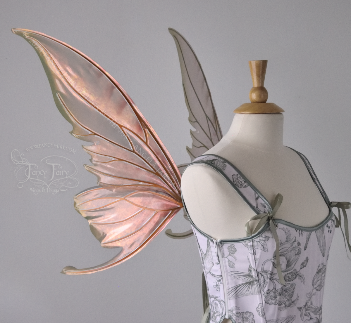 Large coppery iridescent fairy wings with brown and green accents, copper veins, worn with a white & sage green bodice on a dress form, left side view