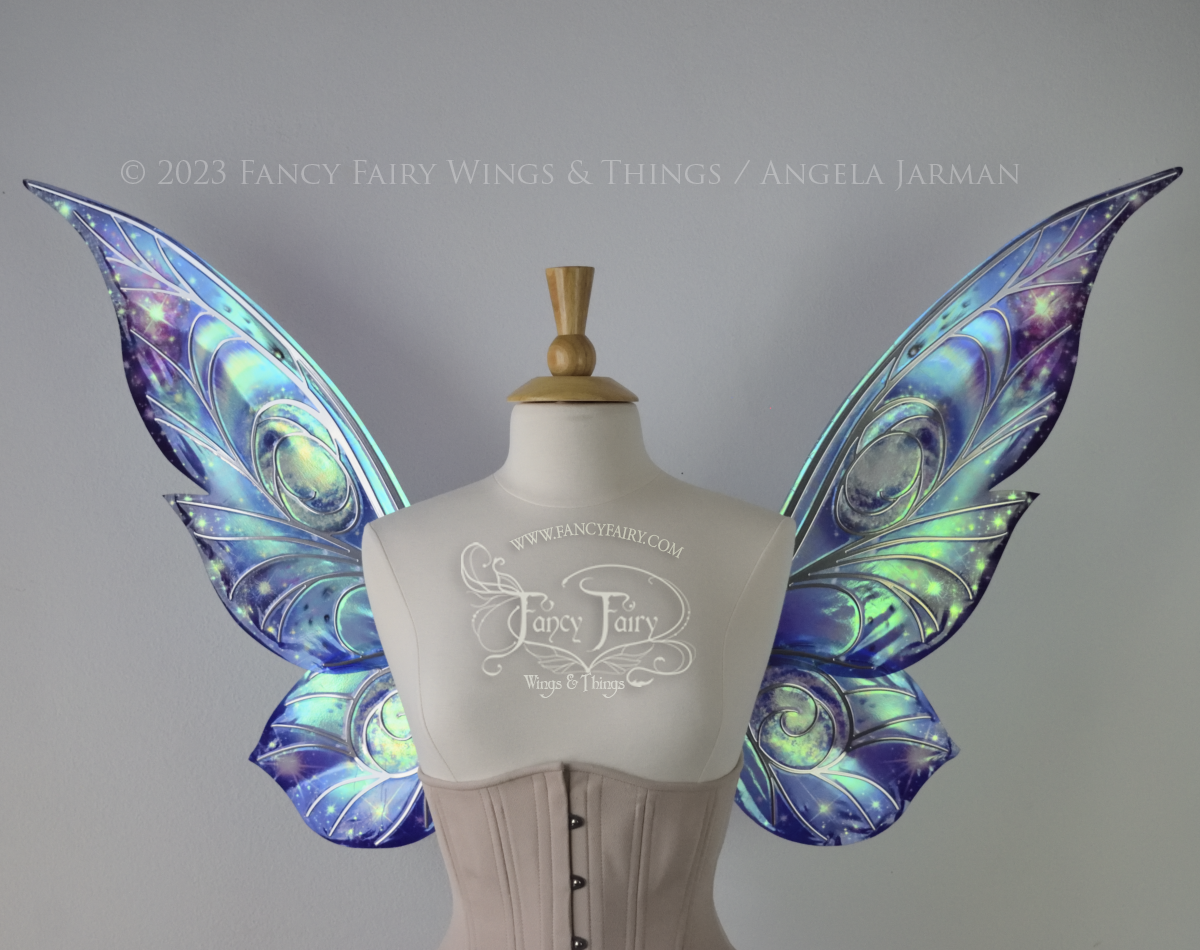 Celestial iridescent fairy wings with blue skies, fuchsia nebulas, auroras and stars, with silver veins, worn on a dress form 