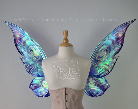 Celestial iridescent fairy wings with blue skies, fuchsia nebulas, auroras and stars, with silver veins, worn on a dress form 