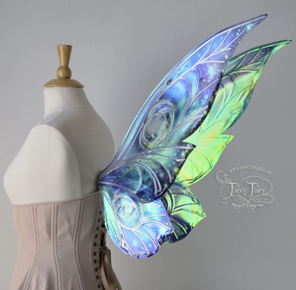 3/4 back view of celestial iridescent fairy wings with blue skies, fuchsia nebulas, auroras and stars, with silver veins, worn on a dress form 