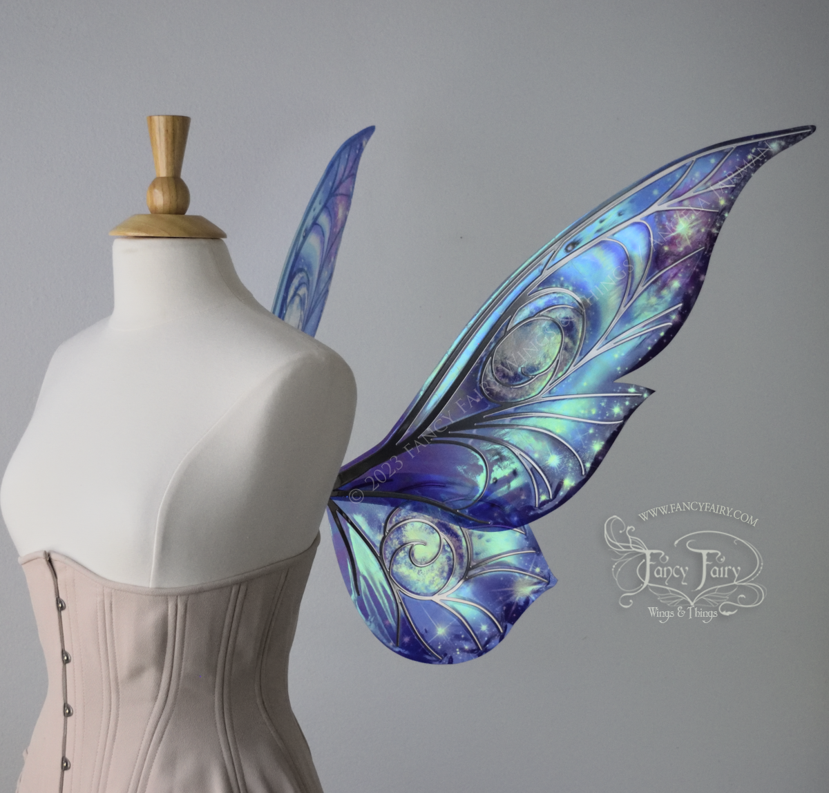 Right side view of celestial iridescent fairy wings with blue skies, fuchsia nebulas, auroras and stars, with silver veins, worn on a dress form 