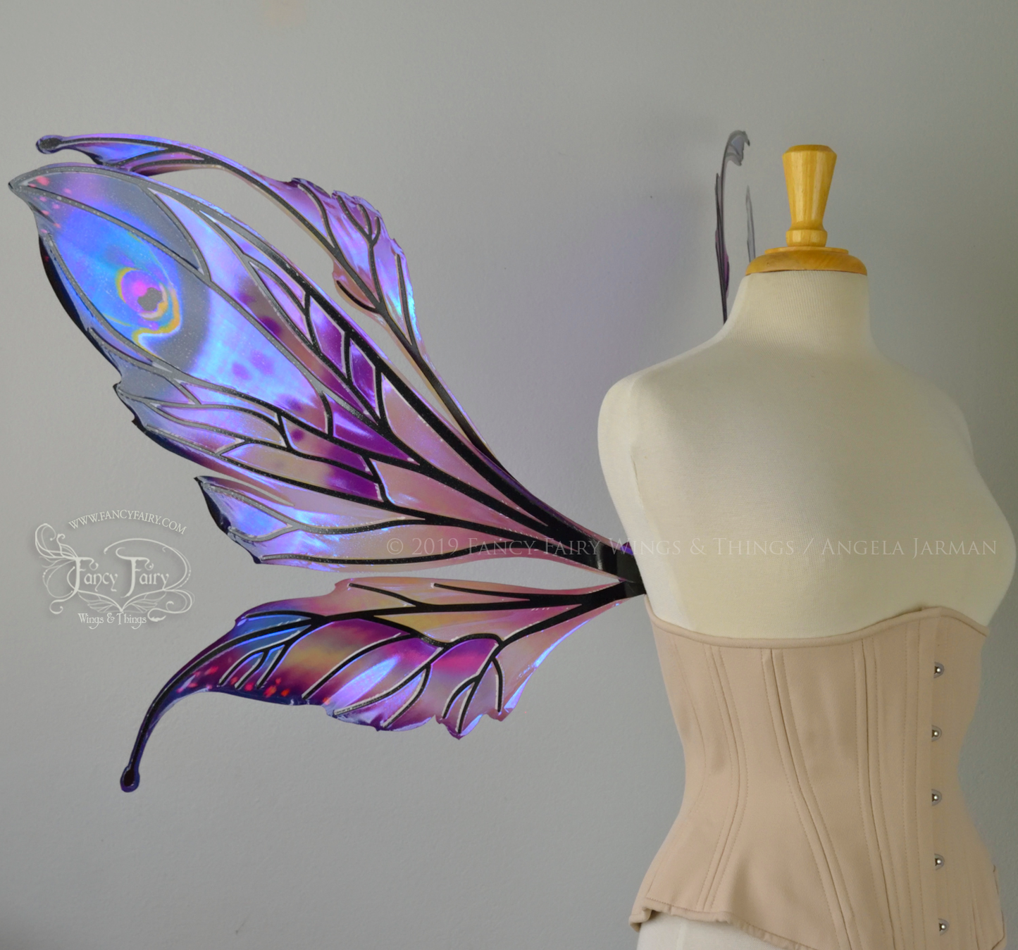 Left side view of a dress form wearing an underbust corset & extra large iridescent fairy wings with mauve purple & blue color pattern 