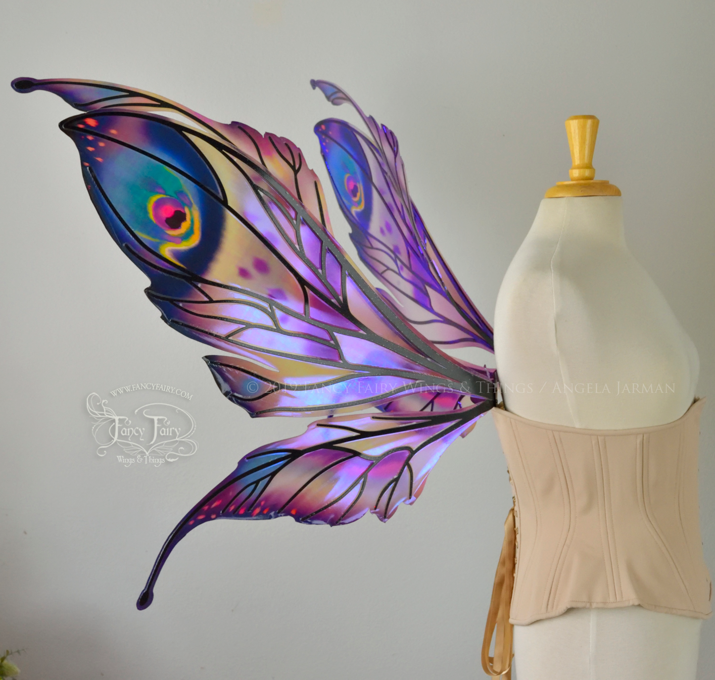 Left side view of a dress form wearing an underbust corset & extra large iridescent fairy wings with mauve purple & blue color pattern 