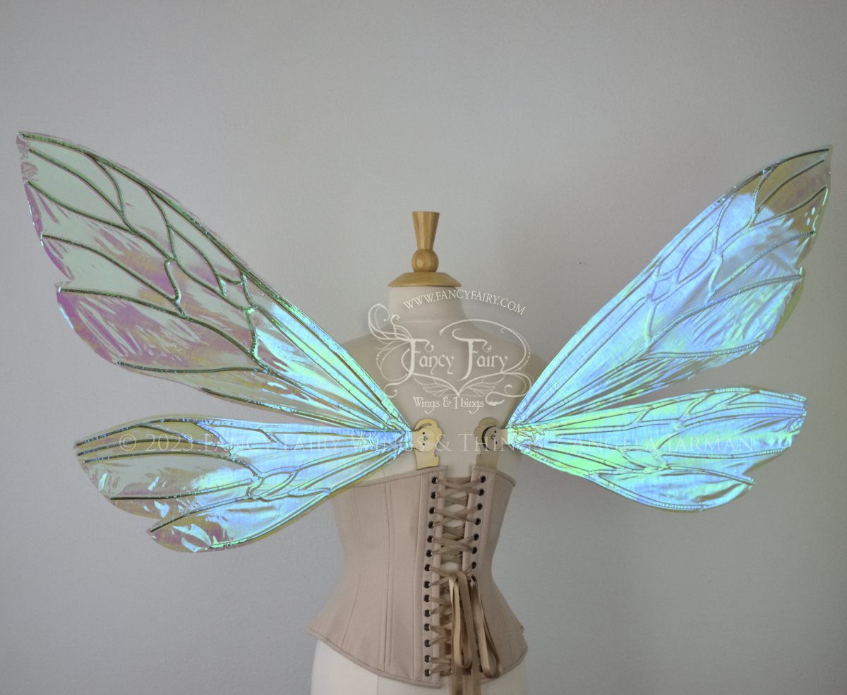 Back view of an ivory dress form wearing an alabaster underbust corset and extra large fairy wings similar to wasp wings, upper and lower panels are both elongated with rounded and slightly pointed tips. They are iridescent green / blue, with gold veins. The background is plain white and my logo and copyright notice are visible.