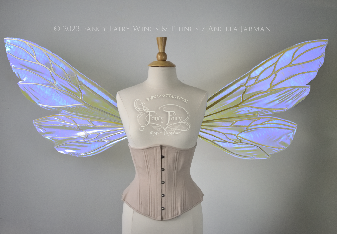 Front view of an ivory dress form wearing an alabaster underbust corset and large fairy wings similar to wasp wings, upper and lower panels are both elongated with rounded and slightly pointed tips. They are iridescent violet / blue, with gold veins. The background is plain white and my logo and copyright notice are visible.