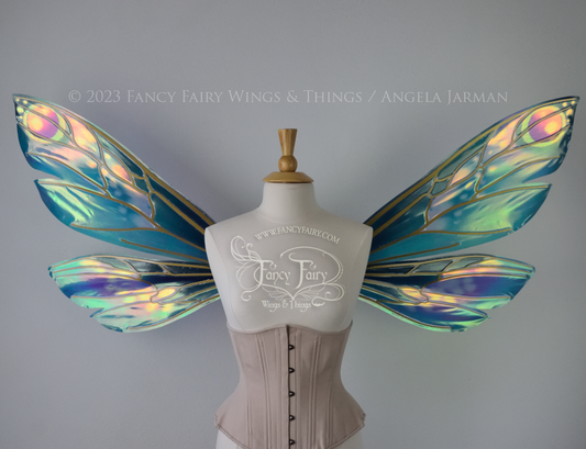 Front view of extra large iridescent fairy wings in various shades of green, teal, blue, lavender with touches of pink, with gold veins, worn on a dress form with underbust corset