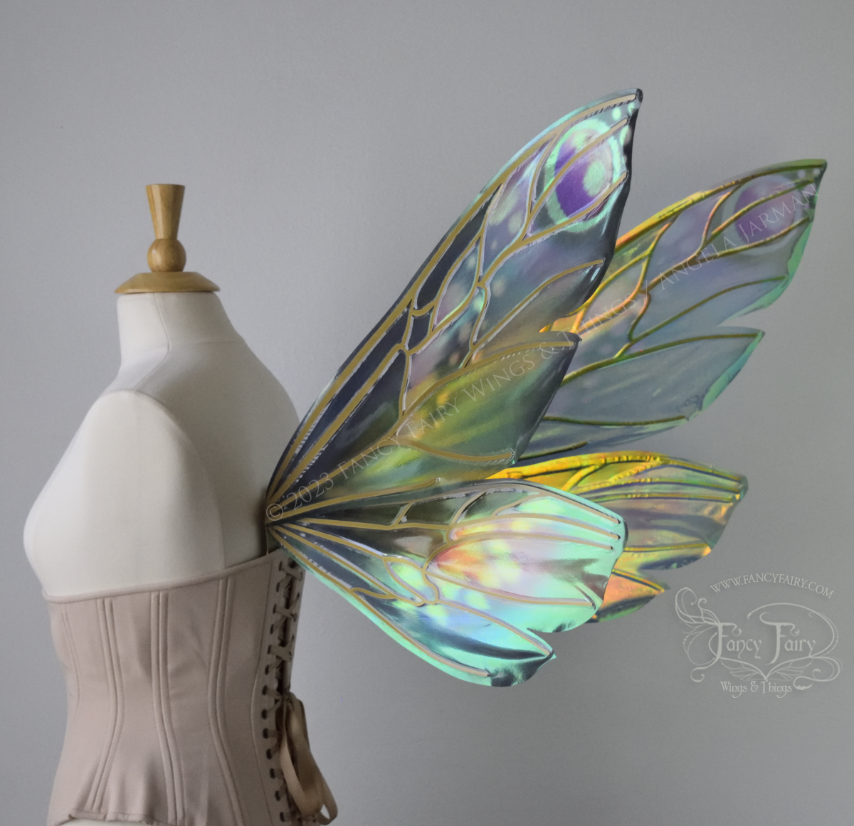 Side 3/4 view of extra large iridescent fairy wings in various shades of green, teal, blue, lavender with touches of pink, with gold veins, worn on a dress form with underbust corset