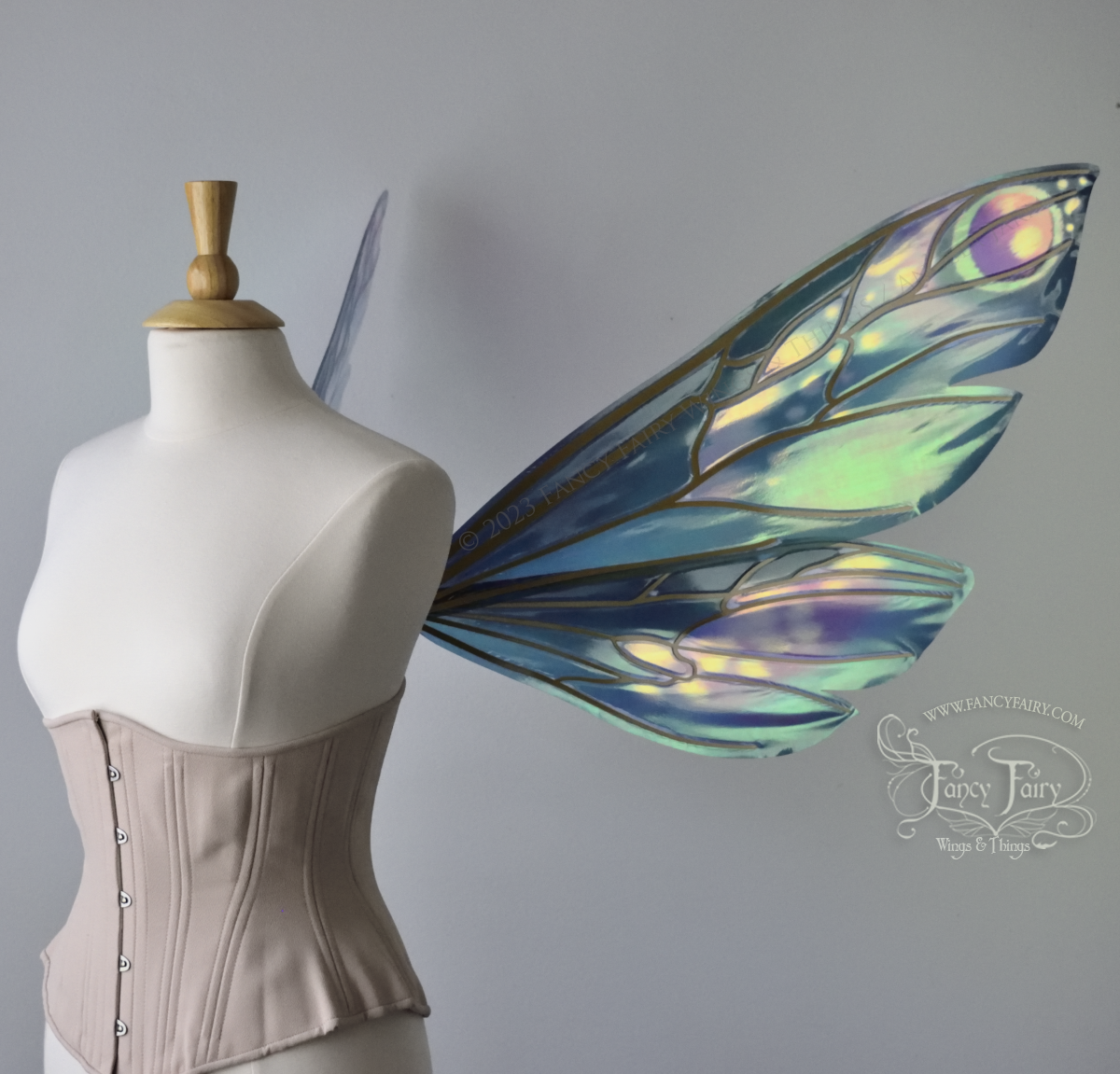Right side view of extra large iridescent fairy wings in various shades of green, teal, blue, lavender with touches of pink, with gold veins, worn on a dress form with underbust corset