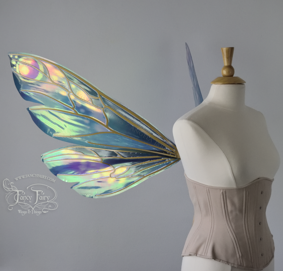 Left side view of extra large iridescent fairy wings in various shades of green, teal, blue, lavender with touches of pink, with gold veins, worn on a dress form with underbust corset