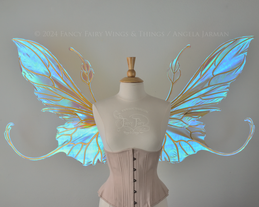 Front view of a dress form wearing an underbust corset & large blue / peach iridescent fairy wings with elongated upper panels & antennae with bottom panels that have a tail curving upwards, gold veins