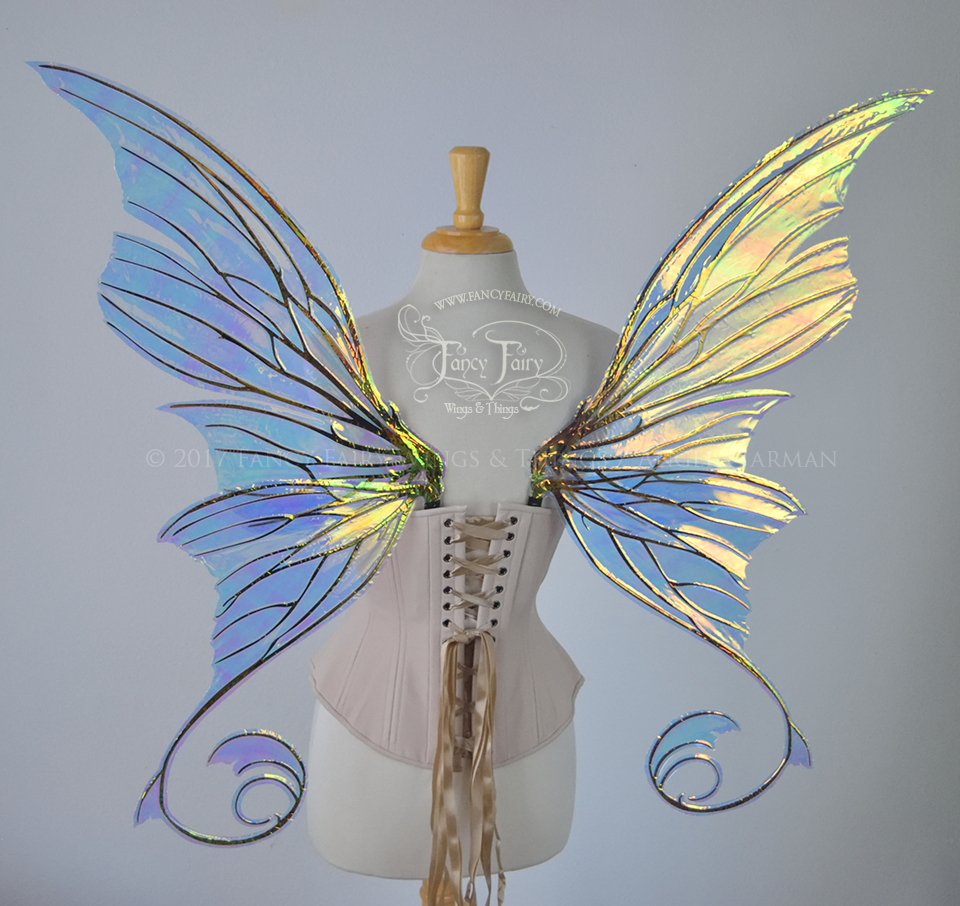 Back view of an ivory dress form wearing an alabaster underbust corset and large fairy wings with lots of intricate veins, some have 'thorns'. The upper panels curve slightly downwards along the top edge with pointy tips, the bottom panels have tails that curve inward toward the body. They are transparent and clear Diamond Fire iridescent, with black veins.