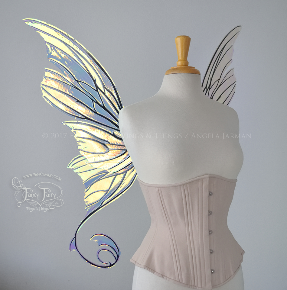 Left side view of an ivory dress form wearing an alabaster underbust corset and large fairy wings with lots of intricate veins, some have 'thorns'. The upper panels curve slightly downwards along the top edge with pointy tips, the bottom panels have tails that curve inward toward the body. They are transparent and clear Diamond Fire iridescent, with black veins.