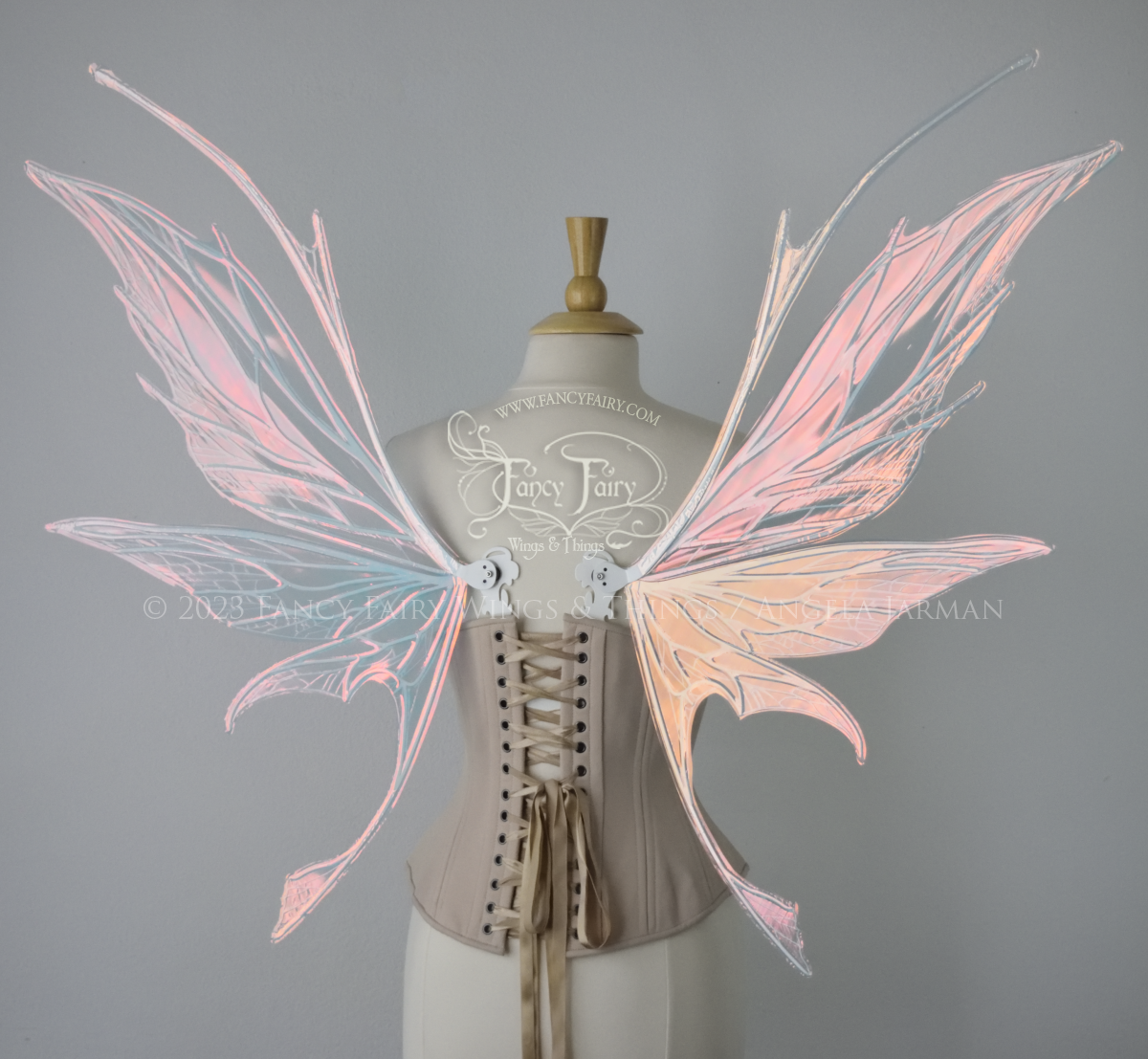 Back view of an ivory dress form wearing an alabaster underbust corset and large pink iridescent fairy wings with antennae on top. Upper panels come to a point, bottom panels have tails. Spikey, detailed white veins, plain white / grey background