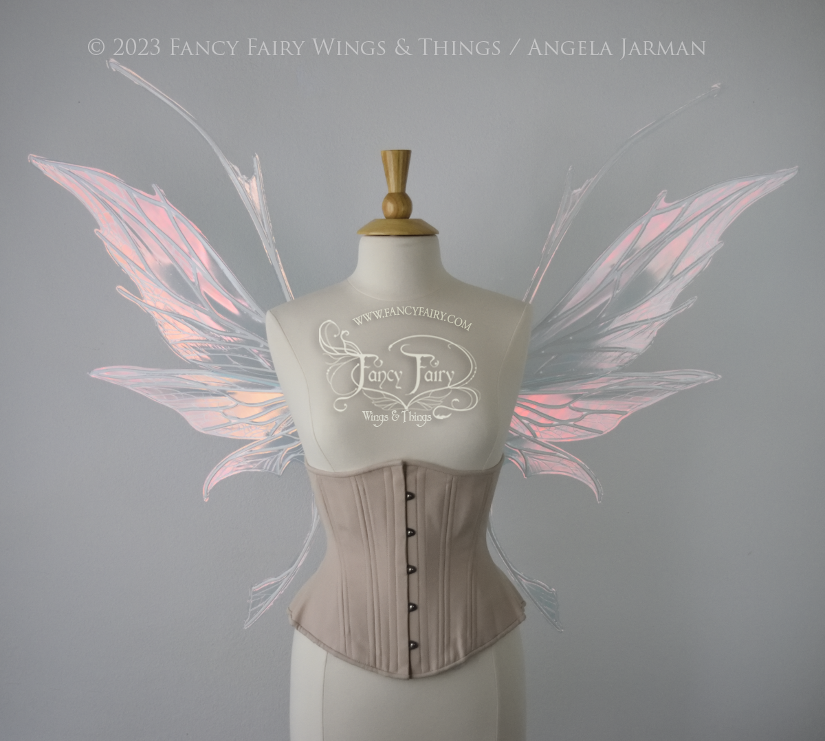 Front view of an ivory dress form wearing an alabaster underbust corset and large pink iridescent fairy wings with antennae on top. Upper panels come to a point, bottom panels have tails. Spikey, detailed white veins, plain white / grey background