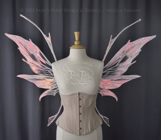Front view of an ivory dress form wearing an alabaster underbust corset and large pink iridescent fairy wings with antennae on top. Upper panels come to a point, bottom panels have tails. Spikey, detailed white veins, dark grey background