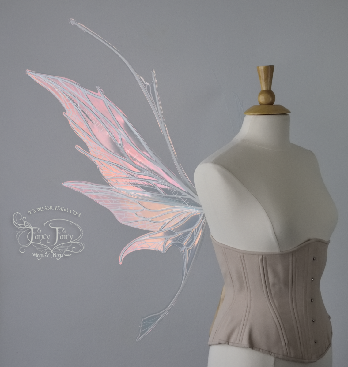 Left side view of an ivory dress form wearing an alabaster underbust corset and large pink iridescent fairy wings with antennae on top. Upper panels come to a point, bottom panels have tails. Spikey, detailed white veins, plain white / grey background