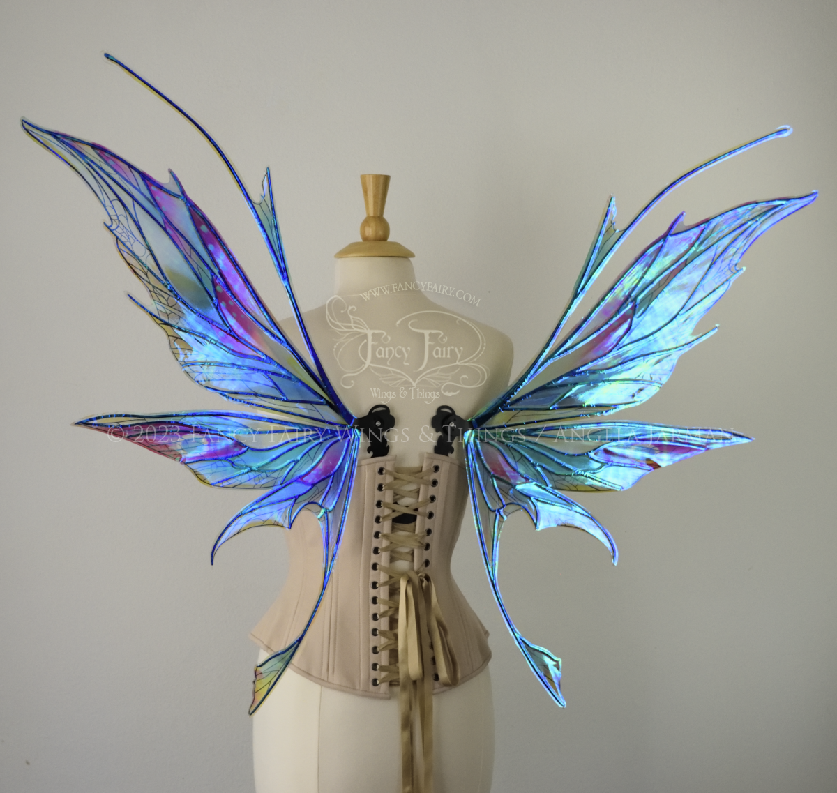 Back view of an ivory dress form wearing an alabaster underbust corset and large multicolor iridescent fairy wings featuring antennae along the top. Upper panels come to a point as do the middle panels, bottom panels have tails. Spikey, detailed veins