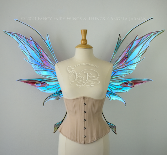 Front view of an ivory dress form wearing an alabaster underbust corset and large multicolor iridescent fairy wings featuring antennae along the top. Upper panels come to a point as do the middle panels, bottom panels have tails. Spikey, detailed veins