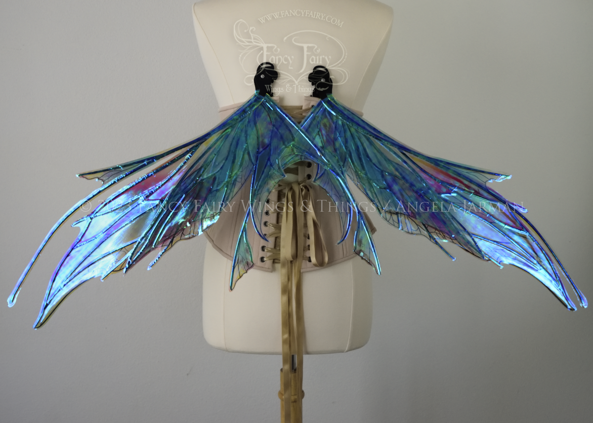 Back view of an ivory dress form wearing an alabaster underbust corset and large multicolor iridescent fairy wings in resting position, featuring antennae along the top. Upper panels come to a point as do the middle panels, bottom panels have tails. Spikey, detailed veins