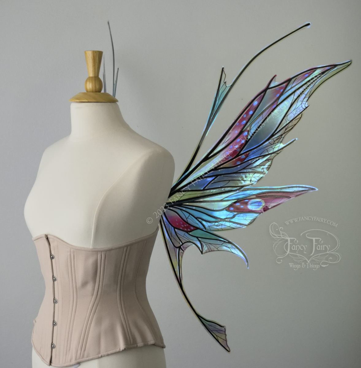 Right side view of an ivory dress form wearing an alabaster underbust corset and large multicolor iridescent fairy wings featuring antennae along the top. Upper panels come to a point as do the middle panels, bottom panels have tails. Spikey, detailed veins