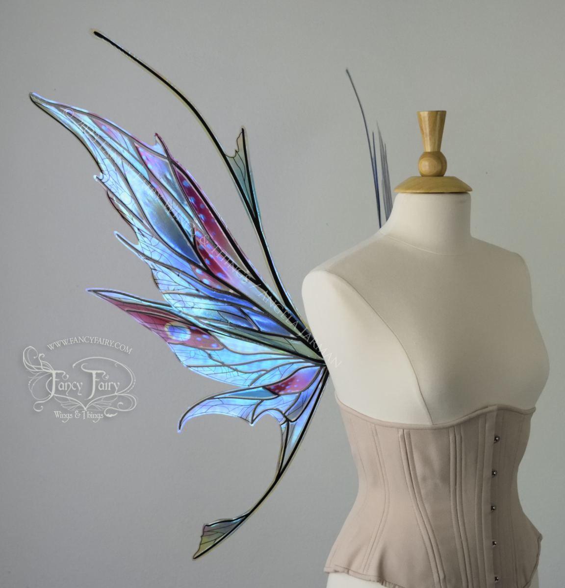 Left side view of an ivory dress form wearing an alabaster underbust corset and large multicolor iridescent fairy wings featuring antennae along the top. Upper panels come to a point as do the middle panels, bottom panels have tails. Spikey, detailed veins