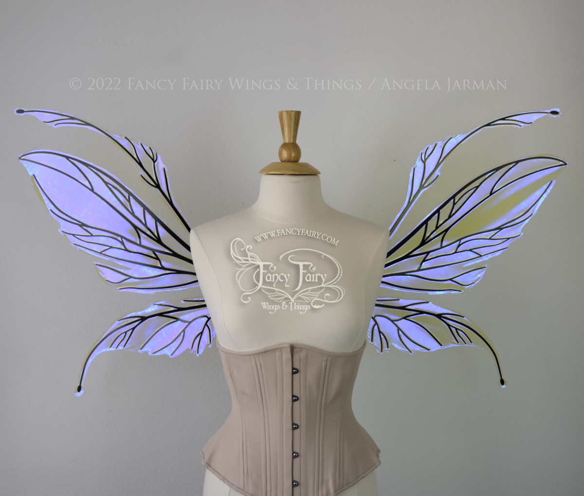 Front view of an dress form wearing an underbust corset and large iridescent violet fairy wings featuring antennae along the top. The upper panels are elongated with semi-pointed tips, the lower panels are smaller with slender tips that curve downward. The veins are black