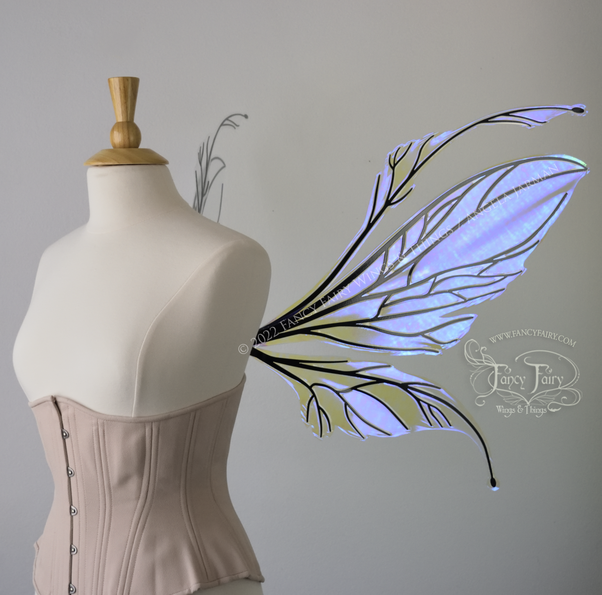 Right side view of an dress form wearing an underbust corset and large iridescent violet fairy wings featuring antennae along the top. The upper panels are elongated with semi-pointed tips, the lower panels are smaller with slender tips that curve downward. The veins are black