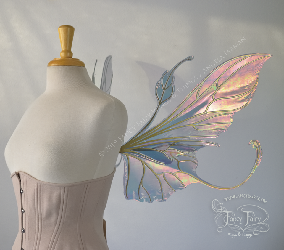 Right side view of an ivory dress form wearing an alabaster underbust corset & large orange/green iridescent fairy wings with elongated upper panels & antennae with bottom panels that have a tail curving upwards, gold veins